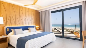 Habitación de hotel con una cama grande, pared de paneles de madera y un balcón con vista a la playa.