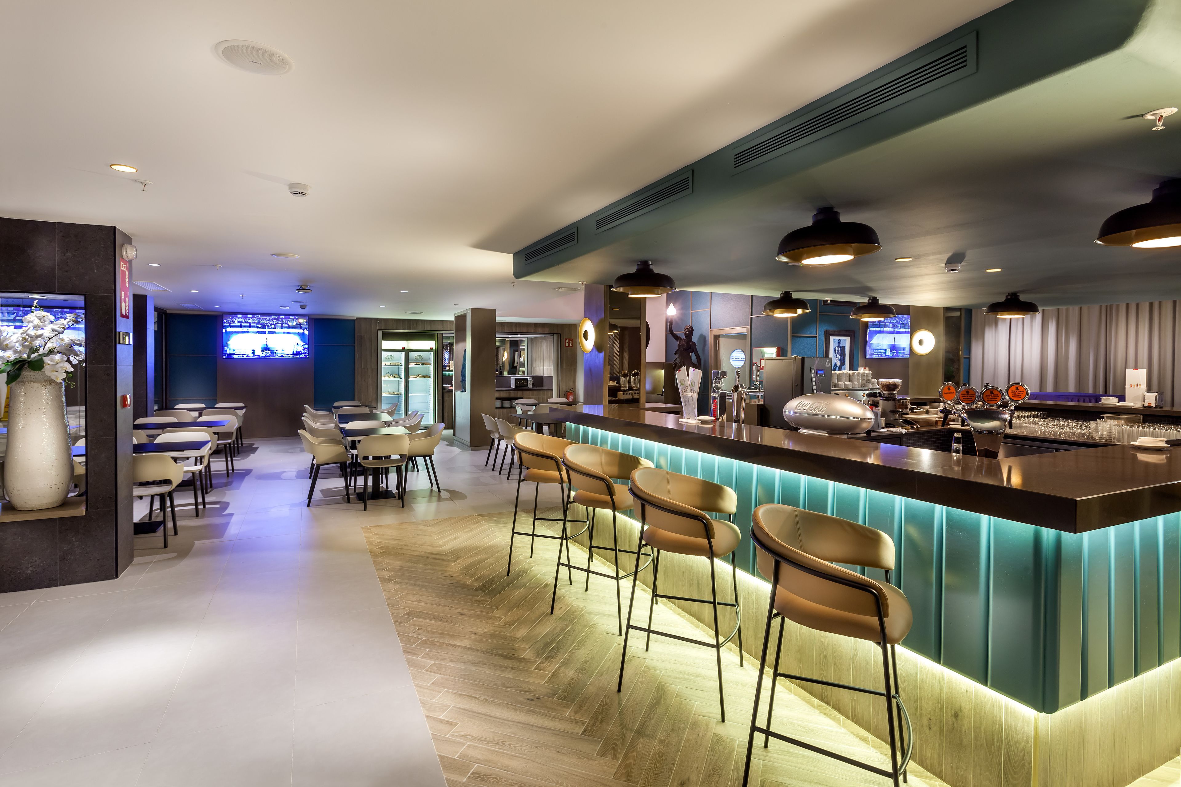 Un espace bar moderne comprenant un comptoir, des tabourets de bar et un coin salon avec des tables et des chaises.