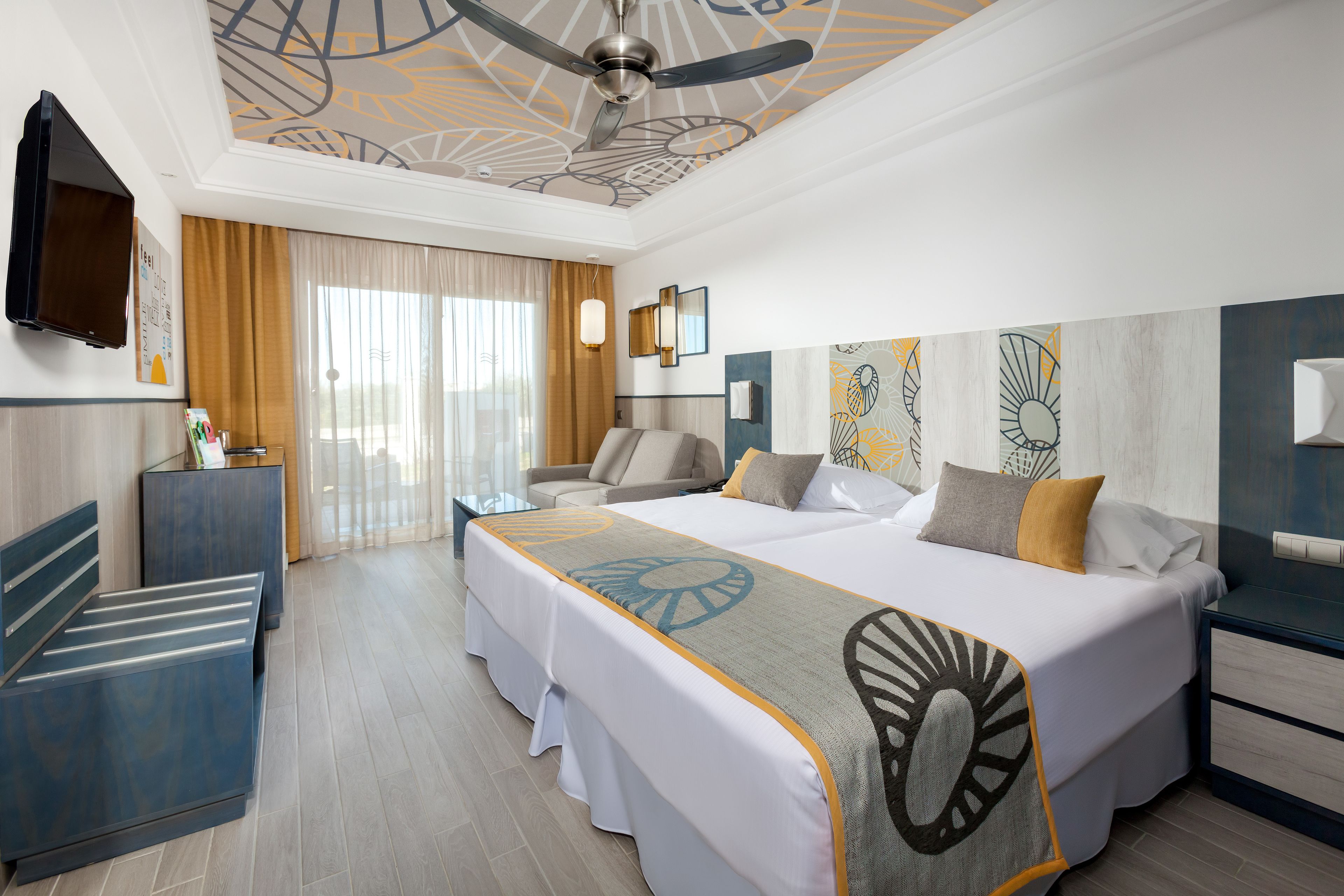 Una habitación de hotel con una cama grande, un escritorio, una silla, un televisor y un ventilador de techo.