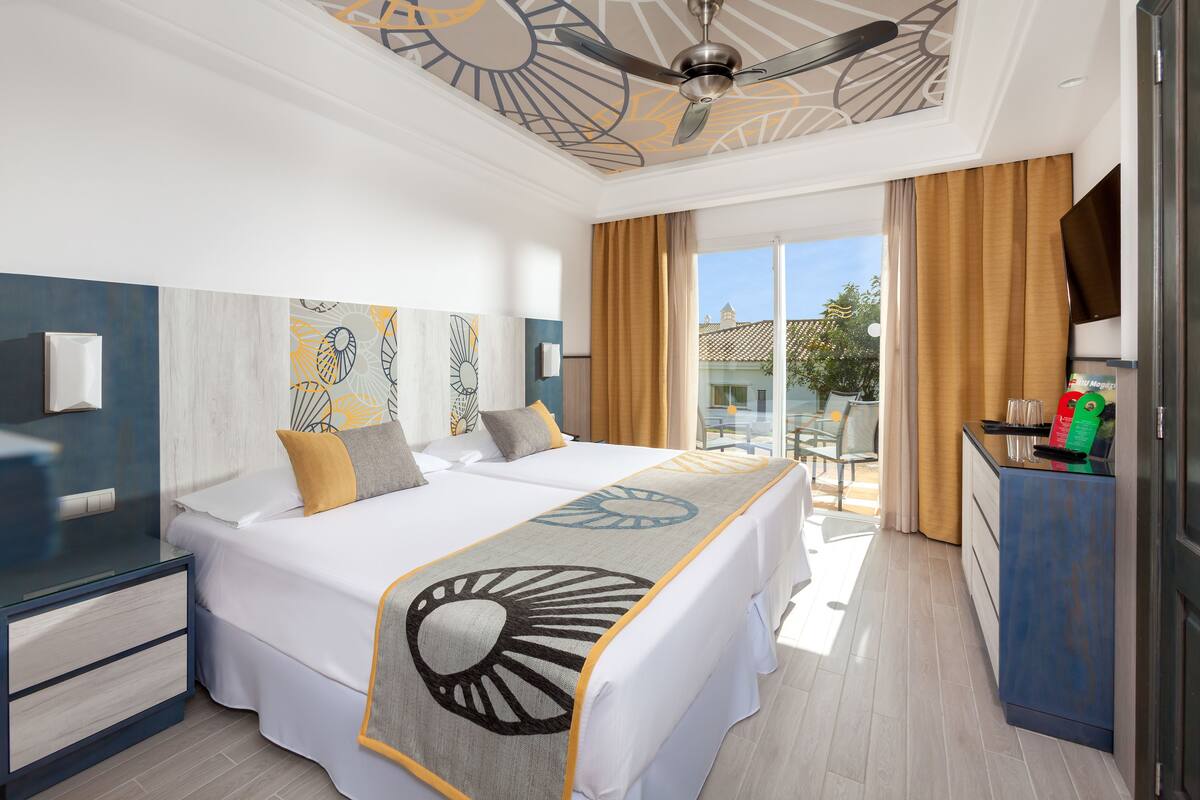 A hotel room with a bed, a desk, a TV, and a balcony with curtains.