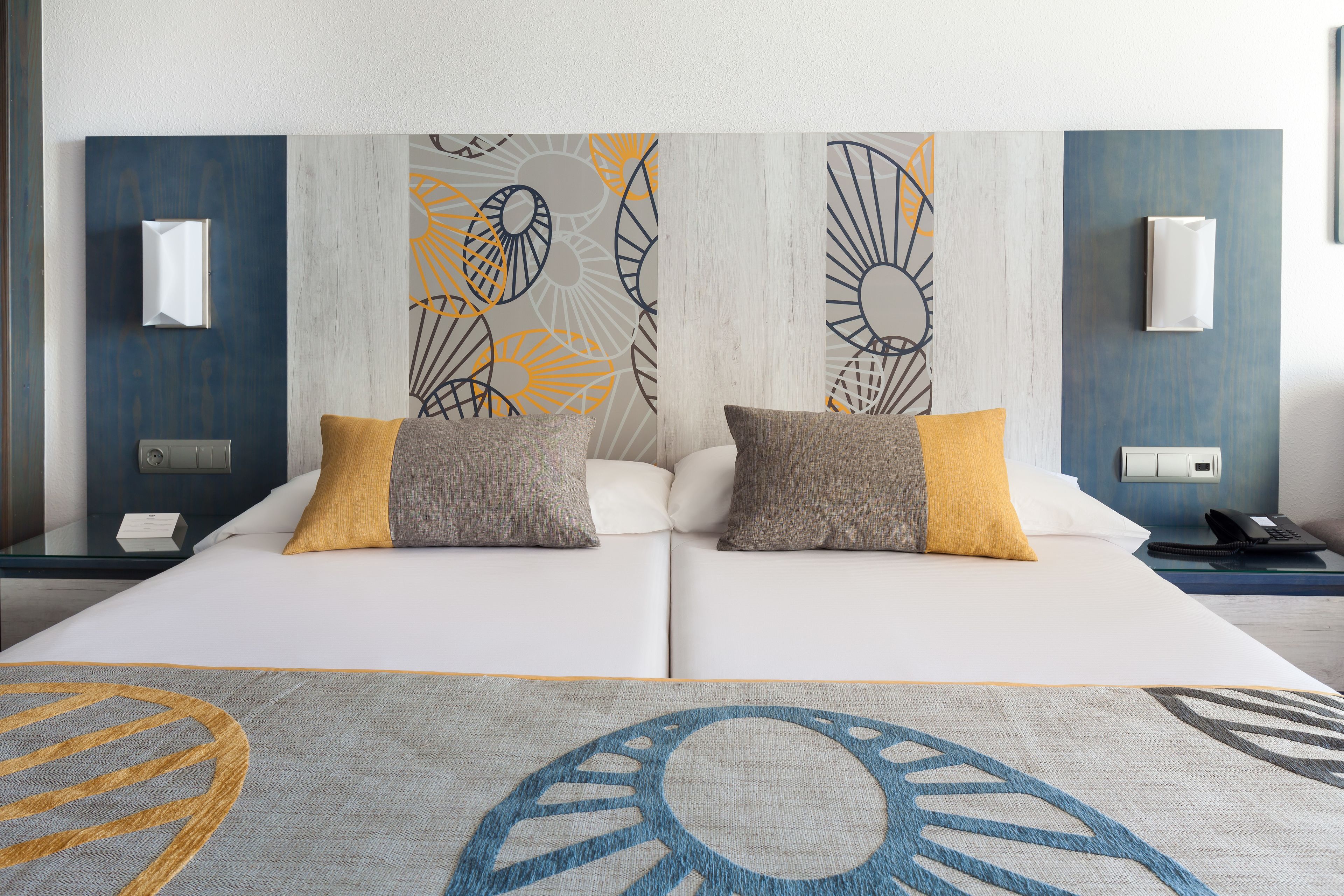 A double bed with two pillows, a bedside table with a phone, and a wall with abstract art.