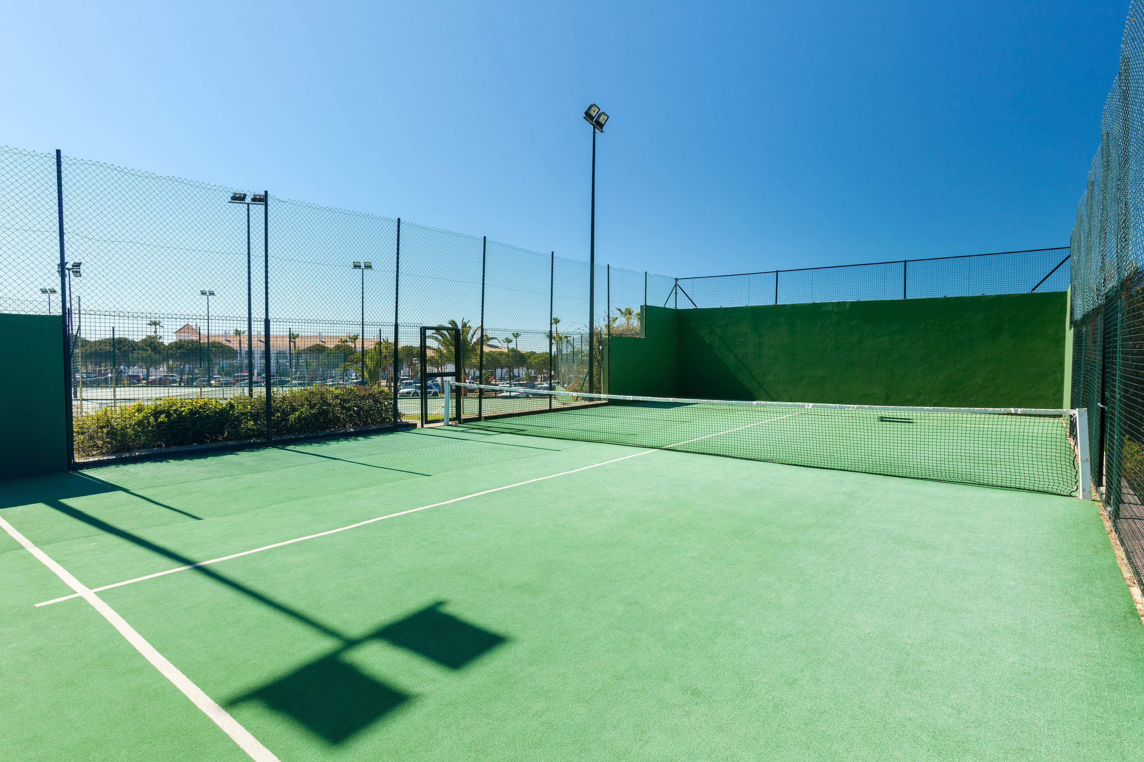 A tennis court with a net, surrounded by a chain-link fence, and equipped with floodlights.