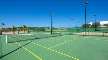 A tennis court with a net, surrounded by a fence, and palm trees in the background.