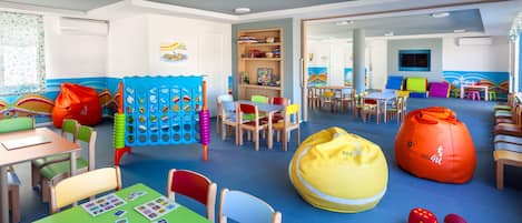 Una sala de juegos infantiles con mesas, sillas, pufs y una estantería.
