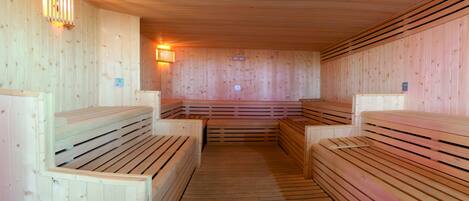 Una sauna con bancos y paredes de madera, equipada con luces y paneles de control empotrados.