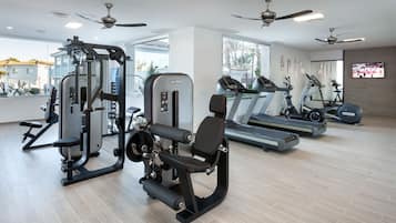 A modern gym with ceiling fans, treadmills, and weight machines.