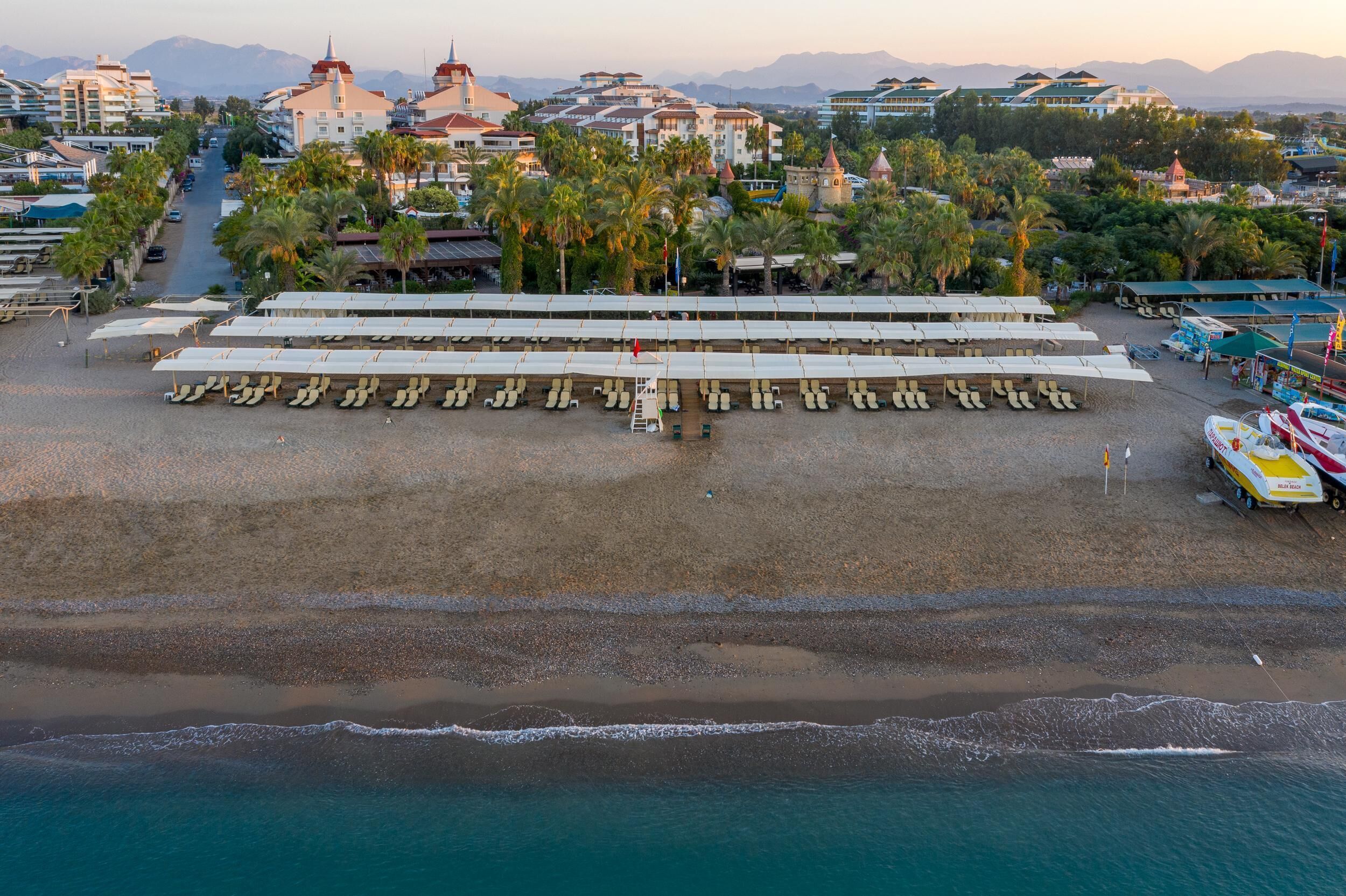 An aerial view of a beach with rows of sun loungers and a boat docked on the right.