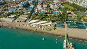An aerial view of a coastal resort with multiple beachside facilities, including sun loungers and umbrellas, and a dock with boats. - Aydinbey Famous Resort - Ultra All Inclusive (Serik)