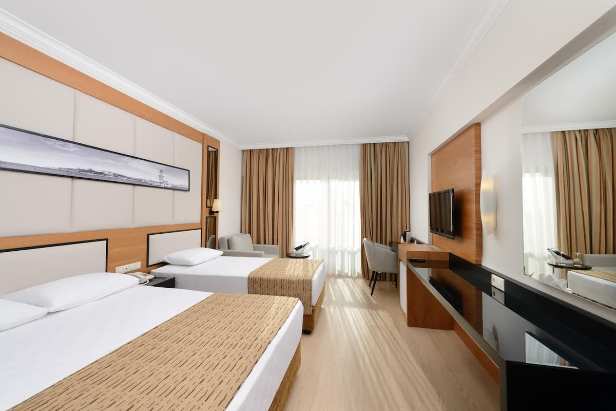 A hotel room with two beds, a desk, a chair, a television, and a large window with curtains.