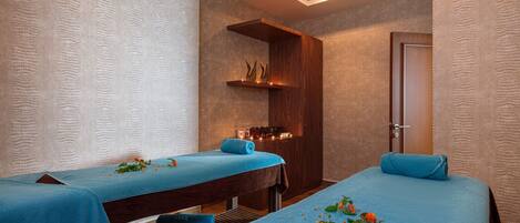 A spa room with two massage tables, wooden benches, a shelf with candles, and a door.