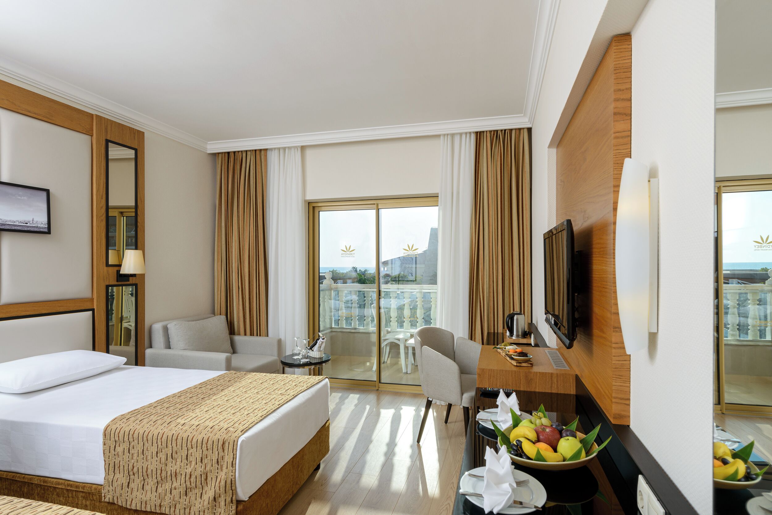 Une chambre d’hôtel comprenant un lit, un bureau avec un ordinateur, une chaise, une petite table avec une lampe, une télévision et un balcon avec vue.