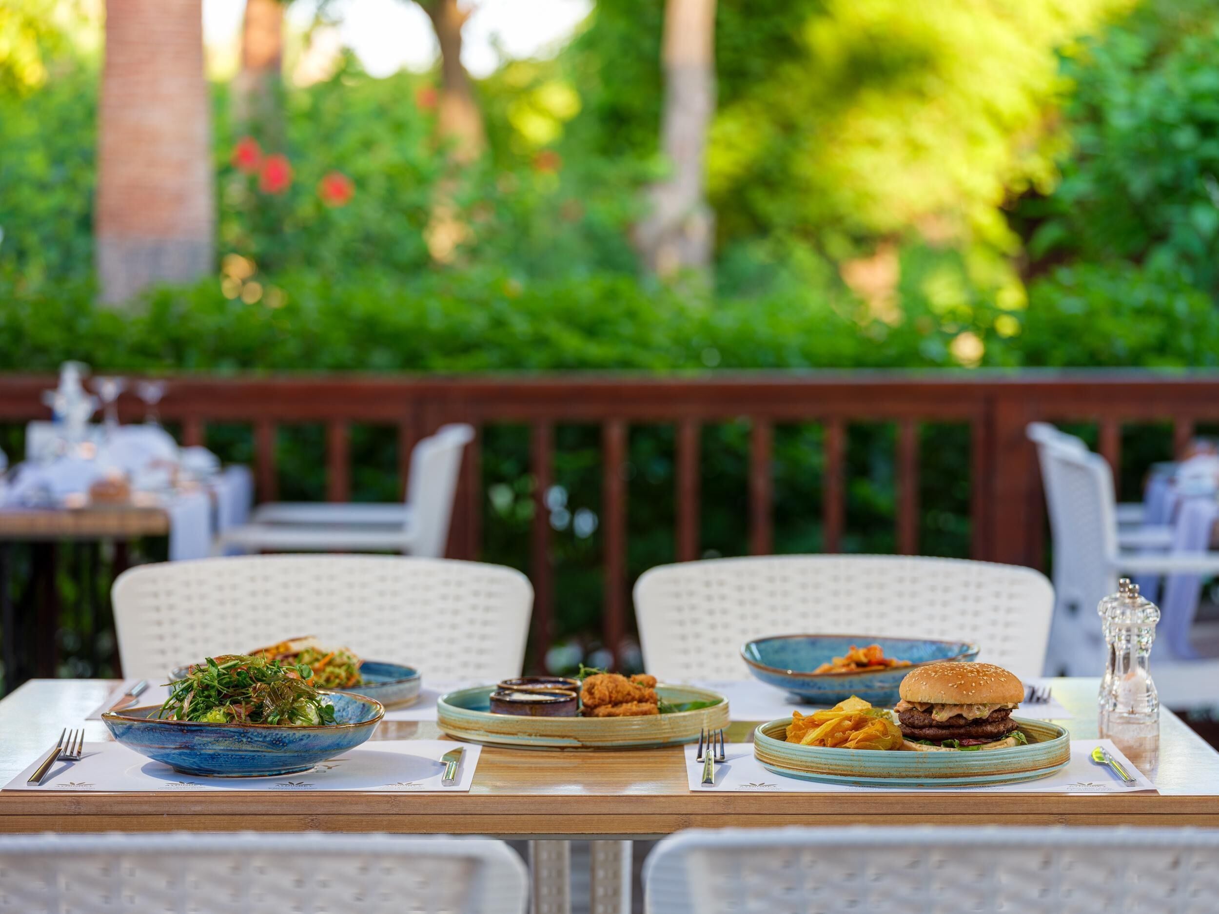 An outdoor dining area with a wooden table set for a meal, surrounded by lush greenery.