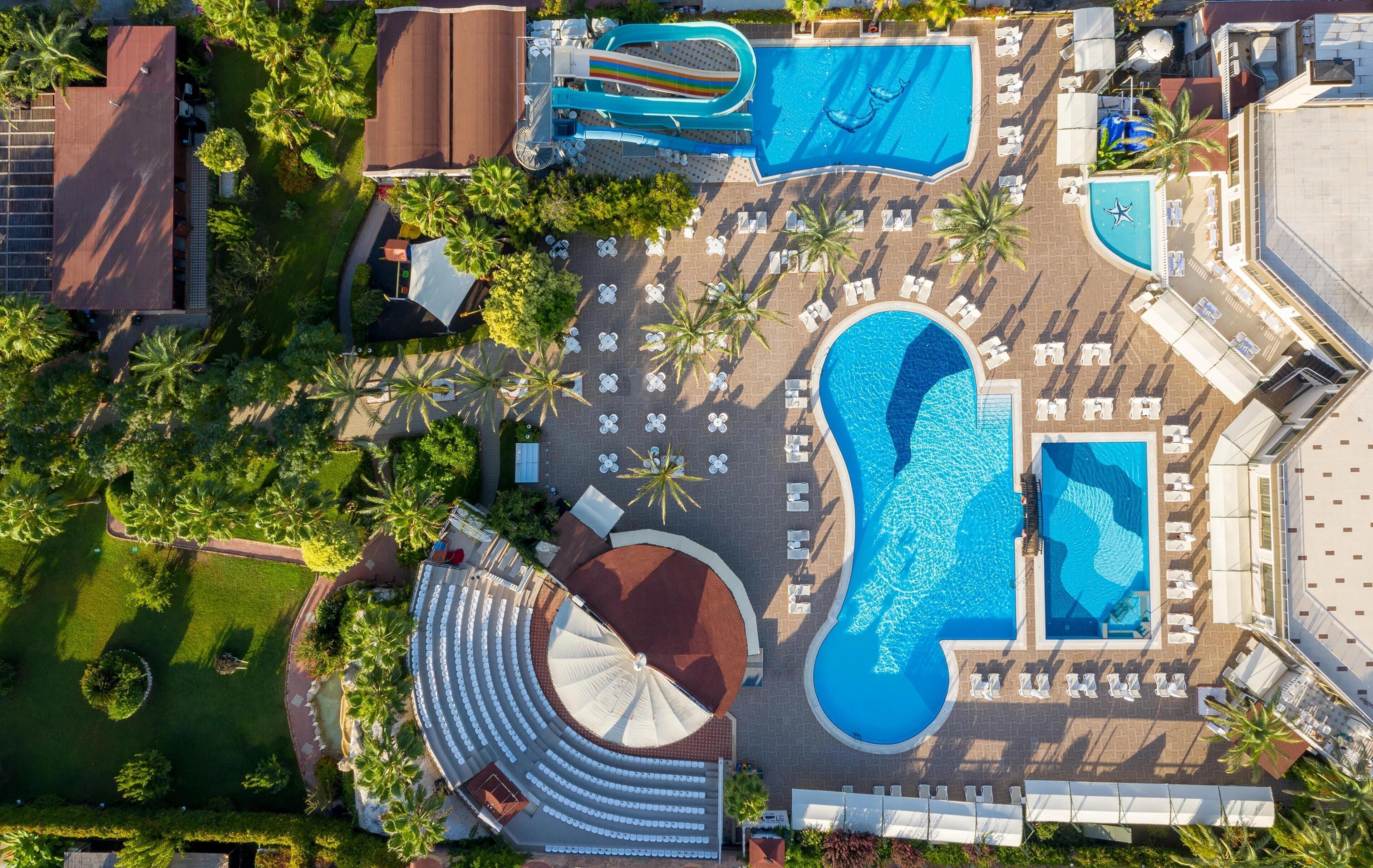 Vista aérea de un complejo turístico con varias piscinas, tumbonas y palmeras.