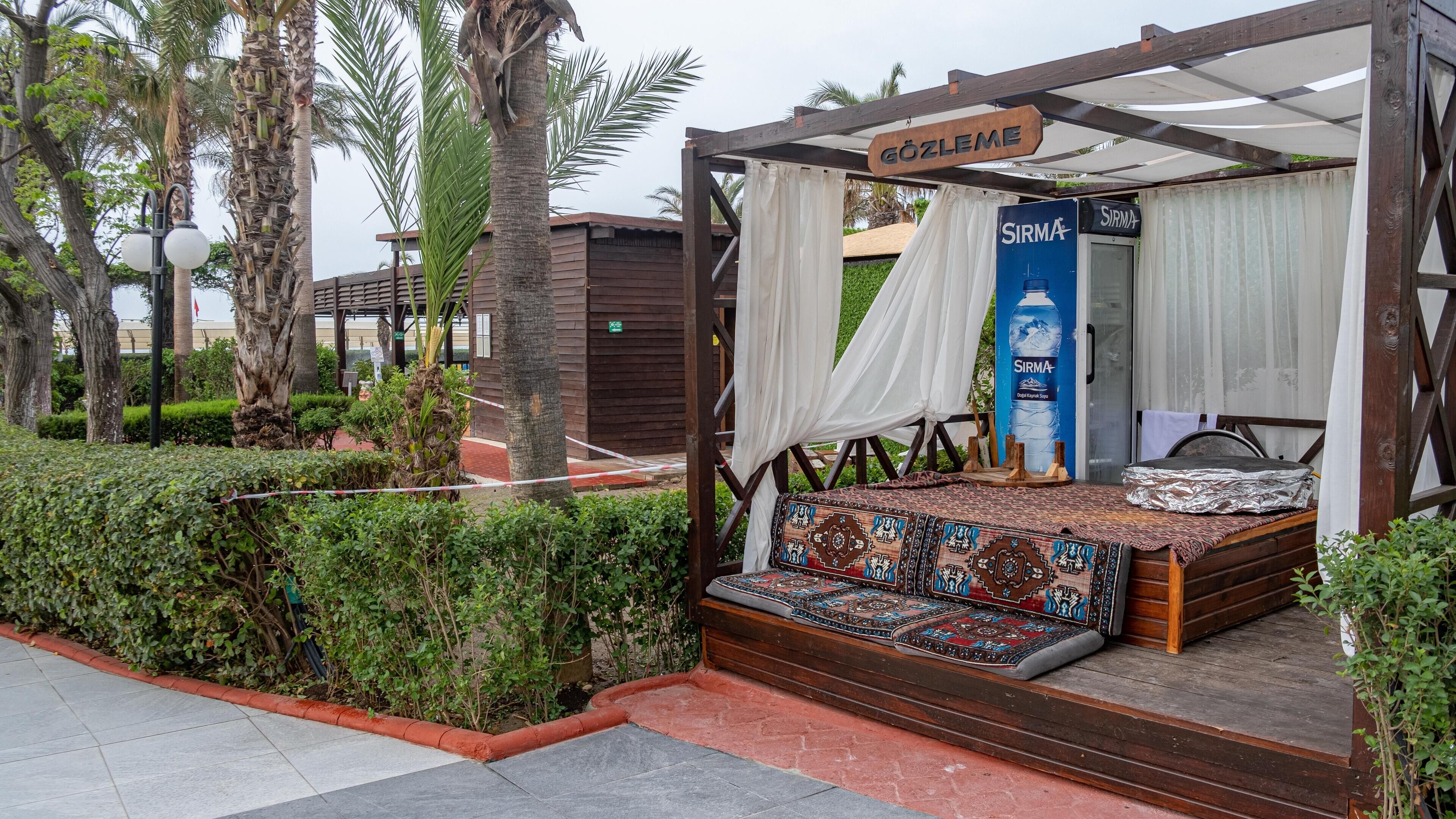 A wooden structure with a bed, a hanging sign reading "GÖZLEM", and a water bottle advertisement.