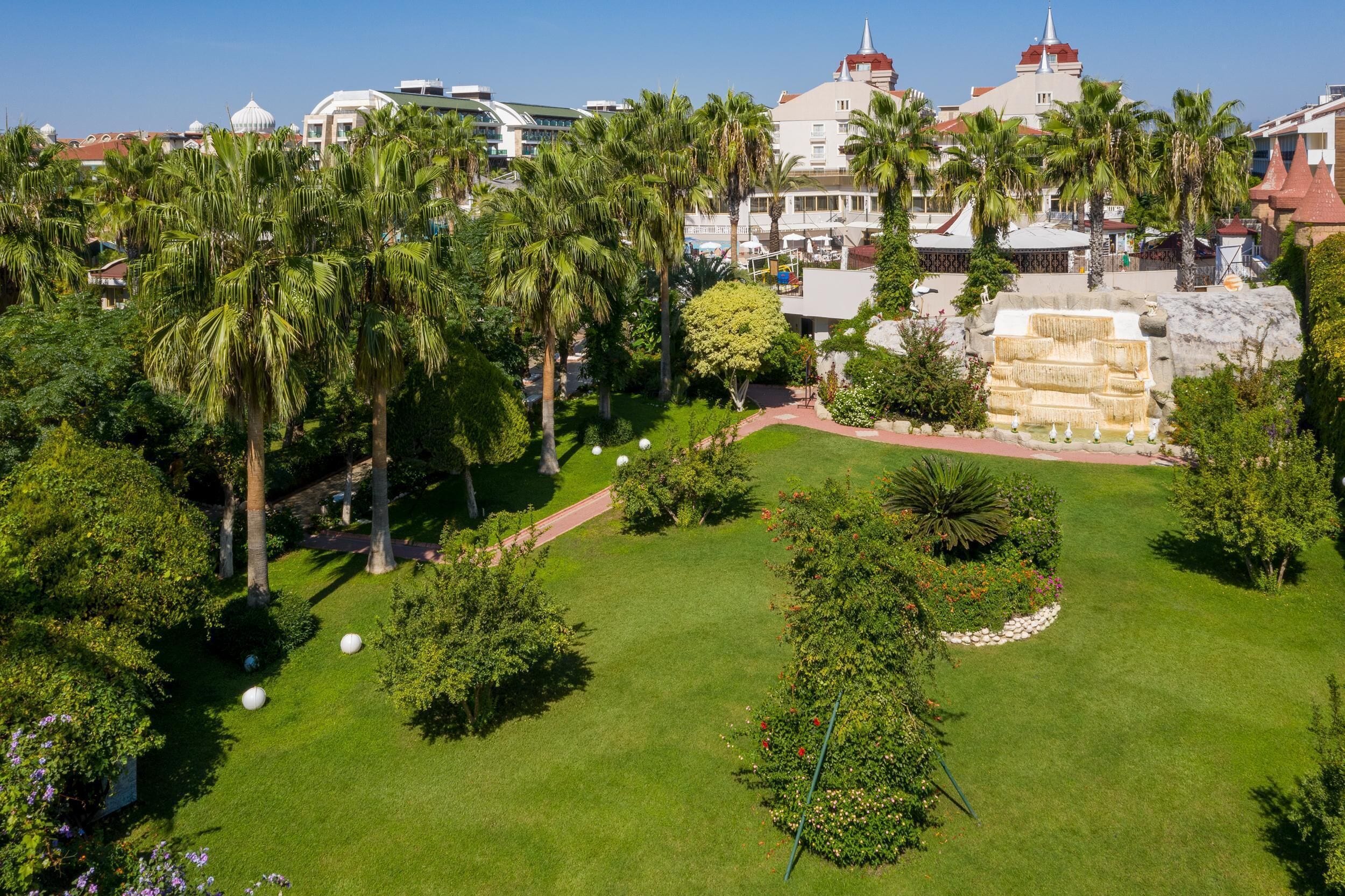 A lush garden with palm trees, a stone fountain, and a pathway.