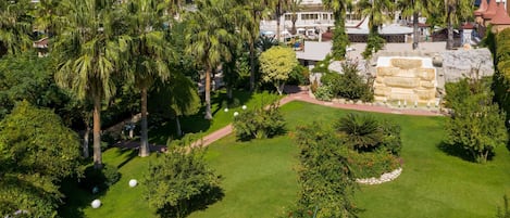 A lush garden with palm trees, a stone fountain, and a pathway.