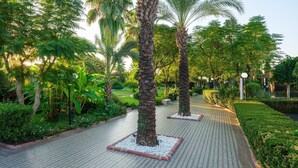 A paved pathway lined with palm trees and lush greenery, leading through a well-maintained garden area. - Aydinbey Famous Resort - Ultra All Inclusive (Serik)