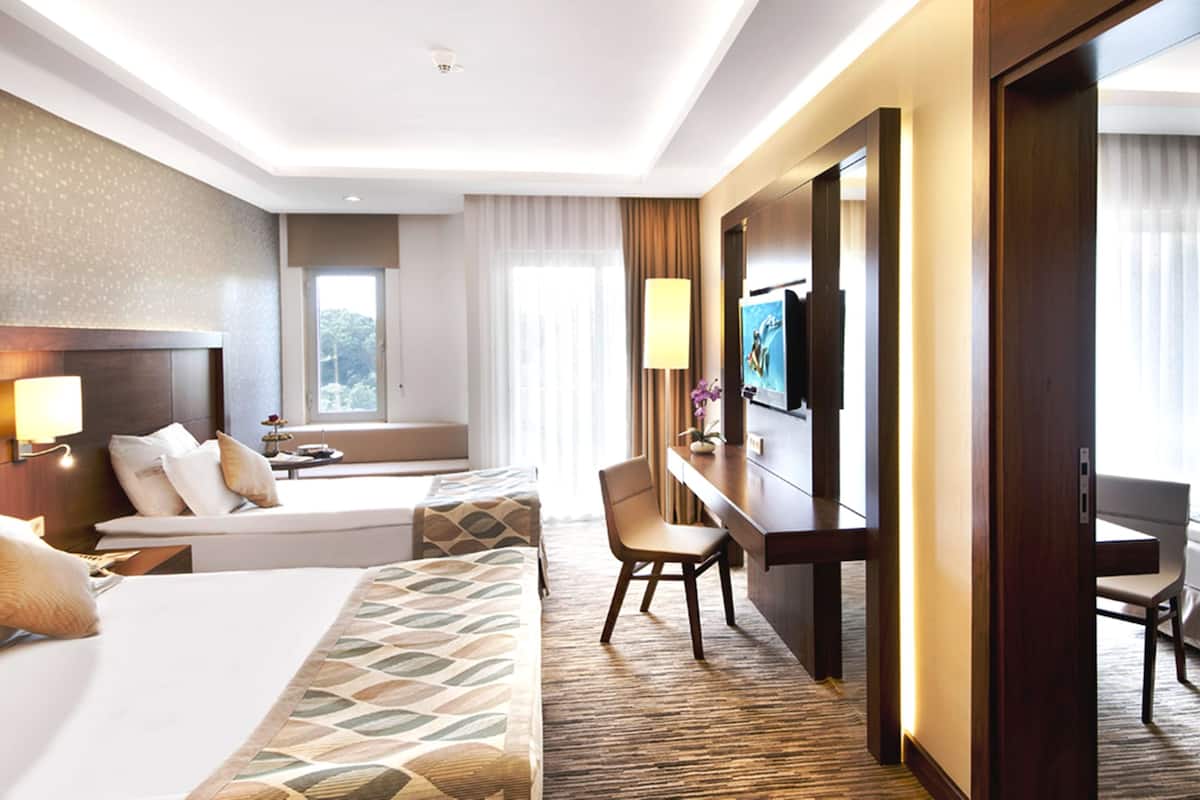 Ein Hotelzimmer mit einem großen Bett, einem Schreibtisch, einem Sessel, einem Fernseher und einem Fenster mit Vorhängen.