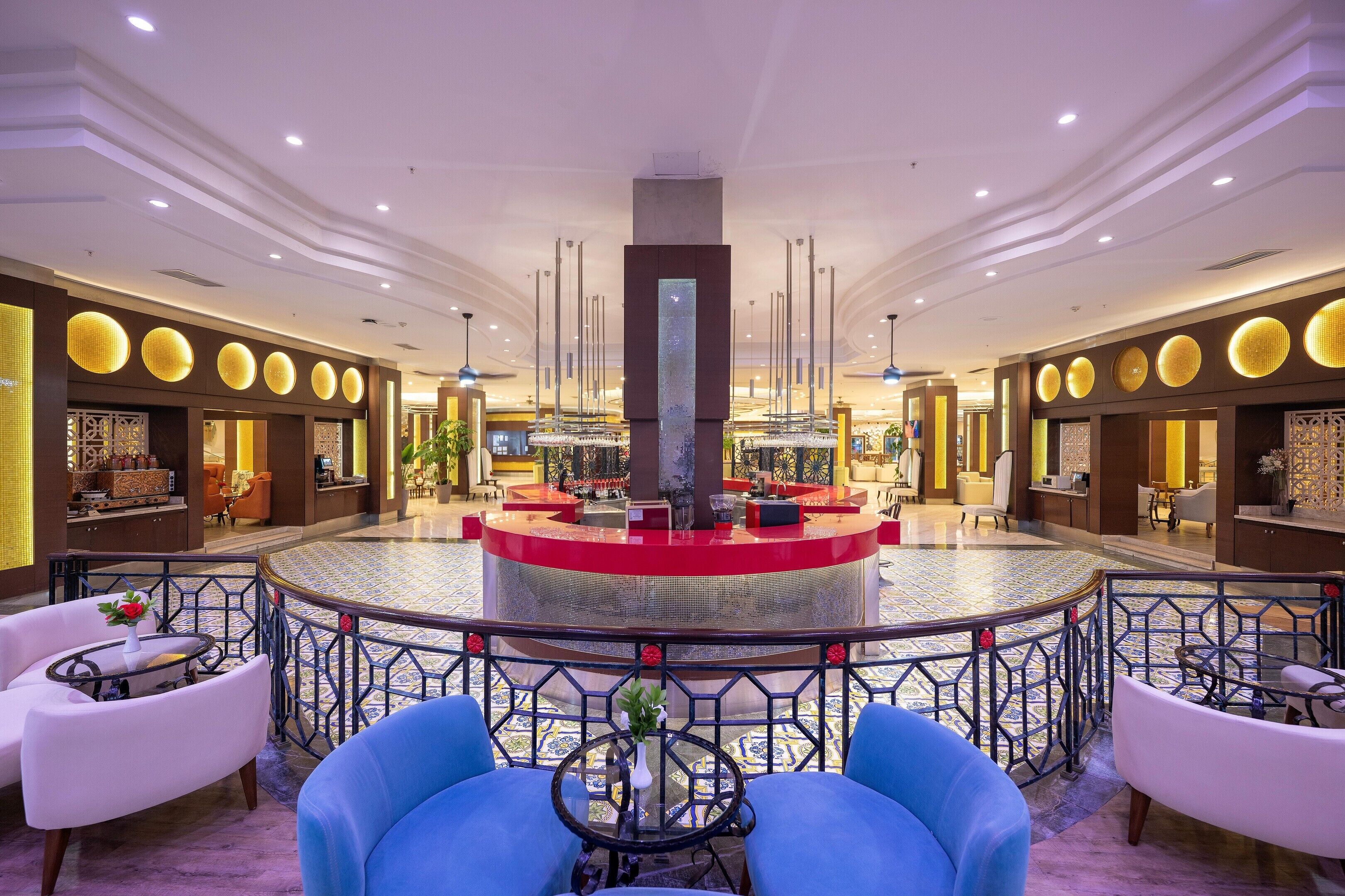 A hotel lobby with a central reception desk, seating areas, and decorative lighting.