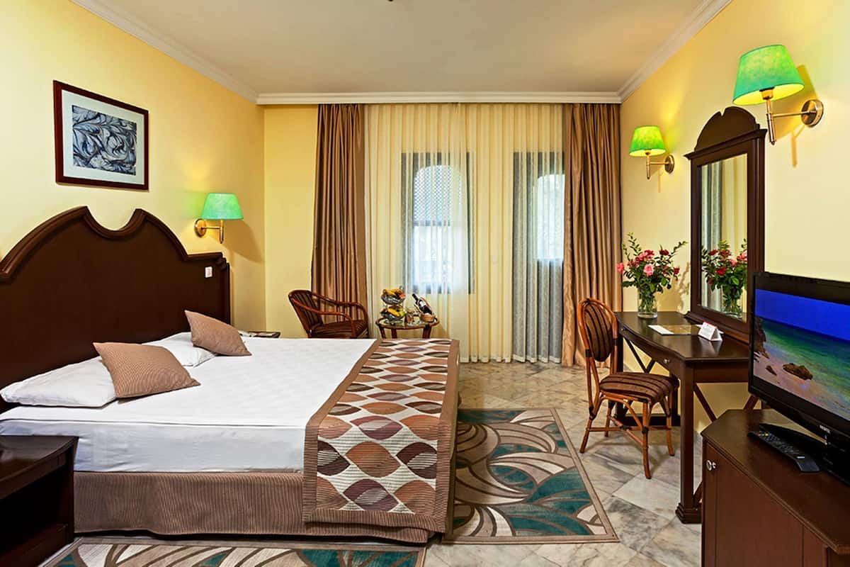Ein Hotelzimmer mit Bett, Schreibtisch, Stuhl, Fernseher und einem Fenster mit Vorhängen.