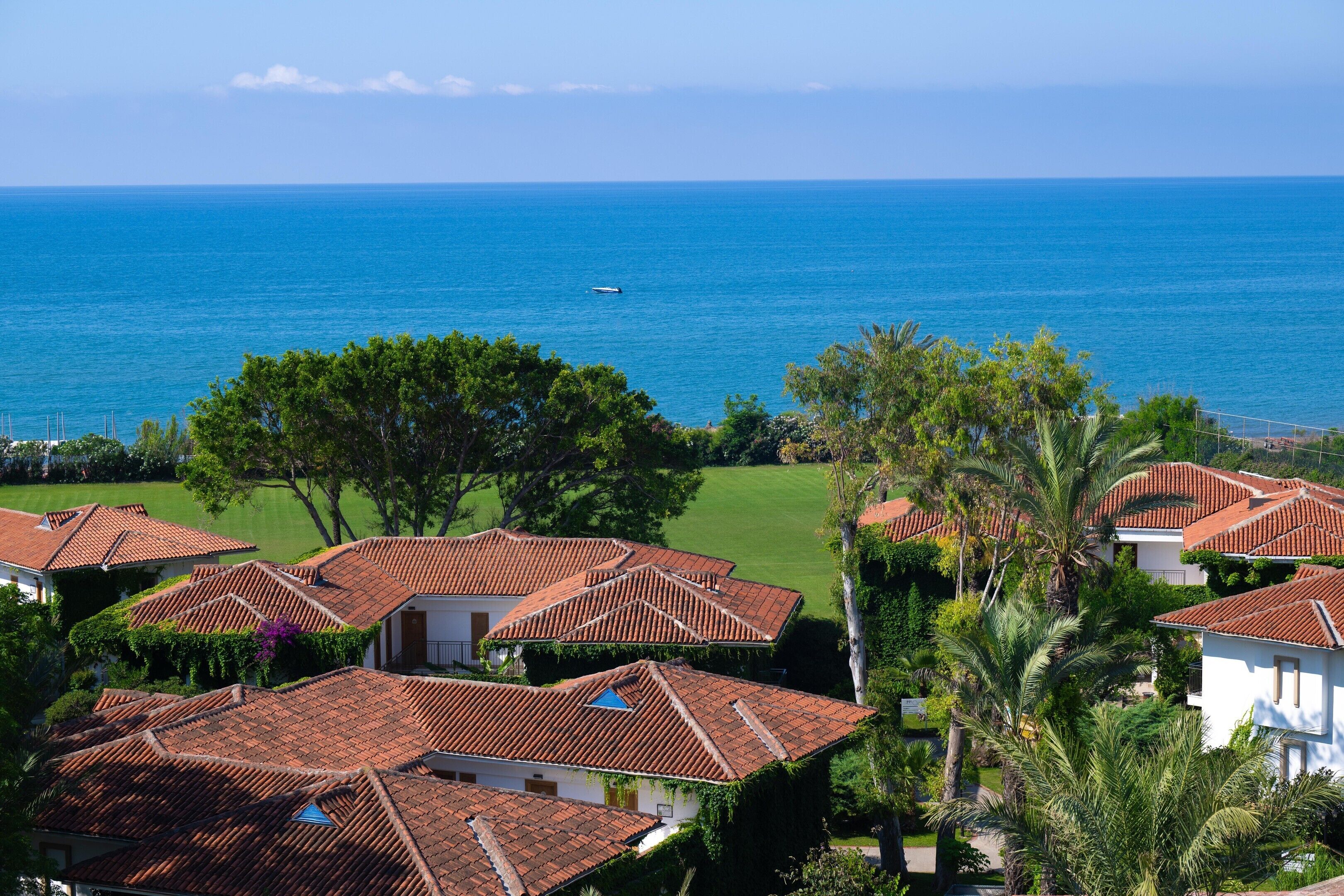 A coastal residential area with houses featuring red-tiled roofs, surrounded by greenery and a view of the sea.