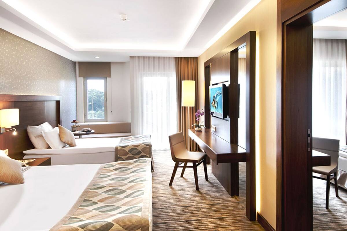 Ein Hotelzimmer mit Bett, Schreibtisch, Stuhl, Fernseher und einem Fenster mit Vorhängen.