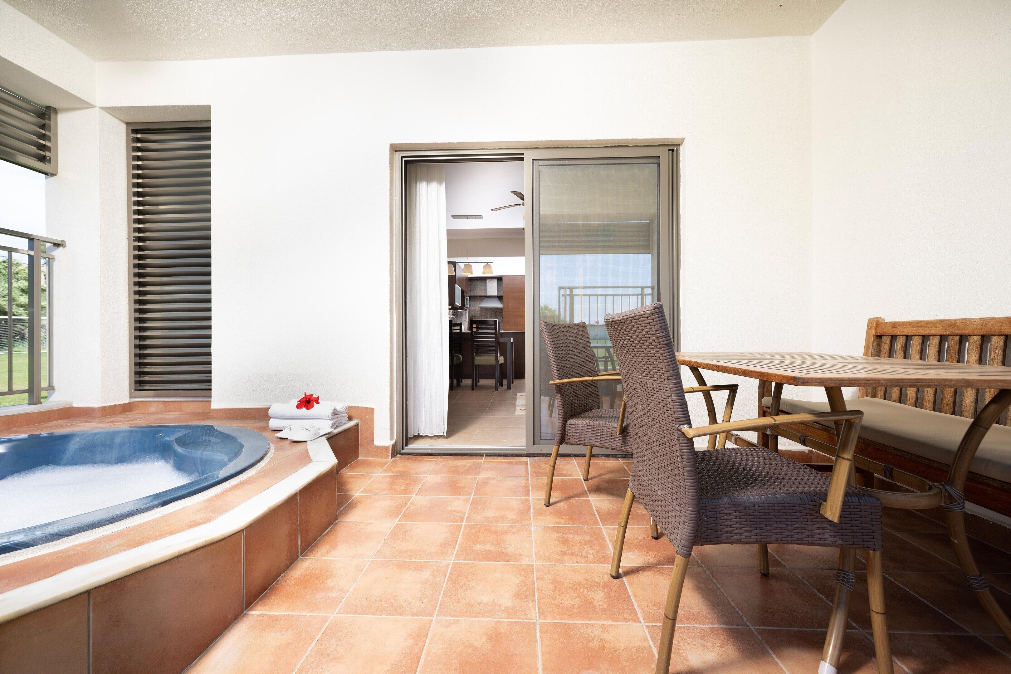 A balcony with a hot tub, a table with chairs, and a view of the interior.