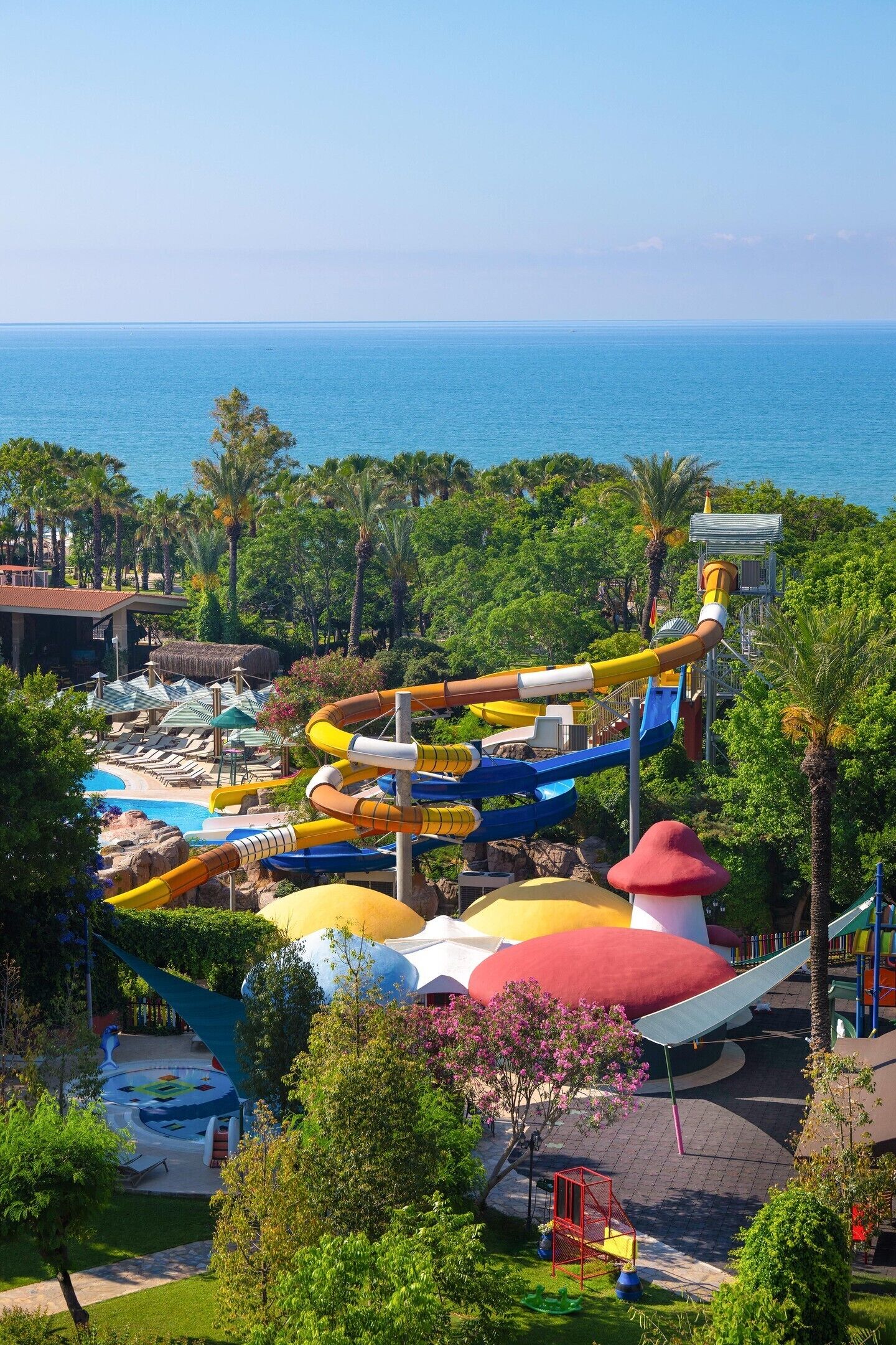 Un parco acquatico con diverse scivoli e un'area piscina, immerso nel verde e con vista sul mare.