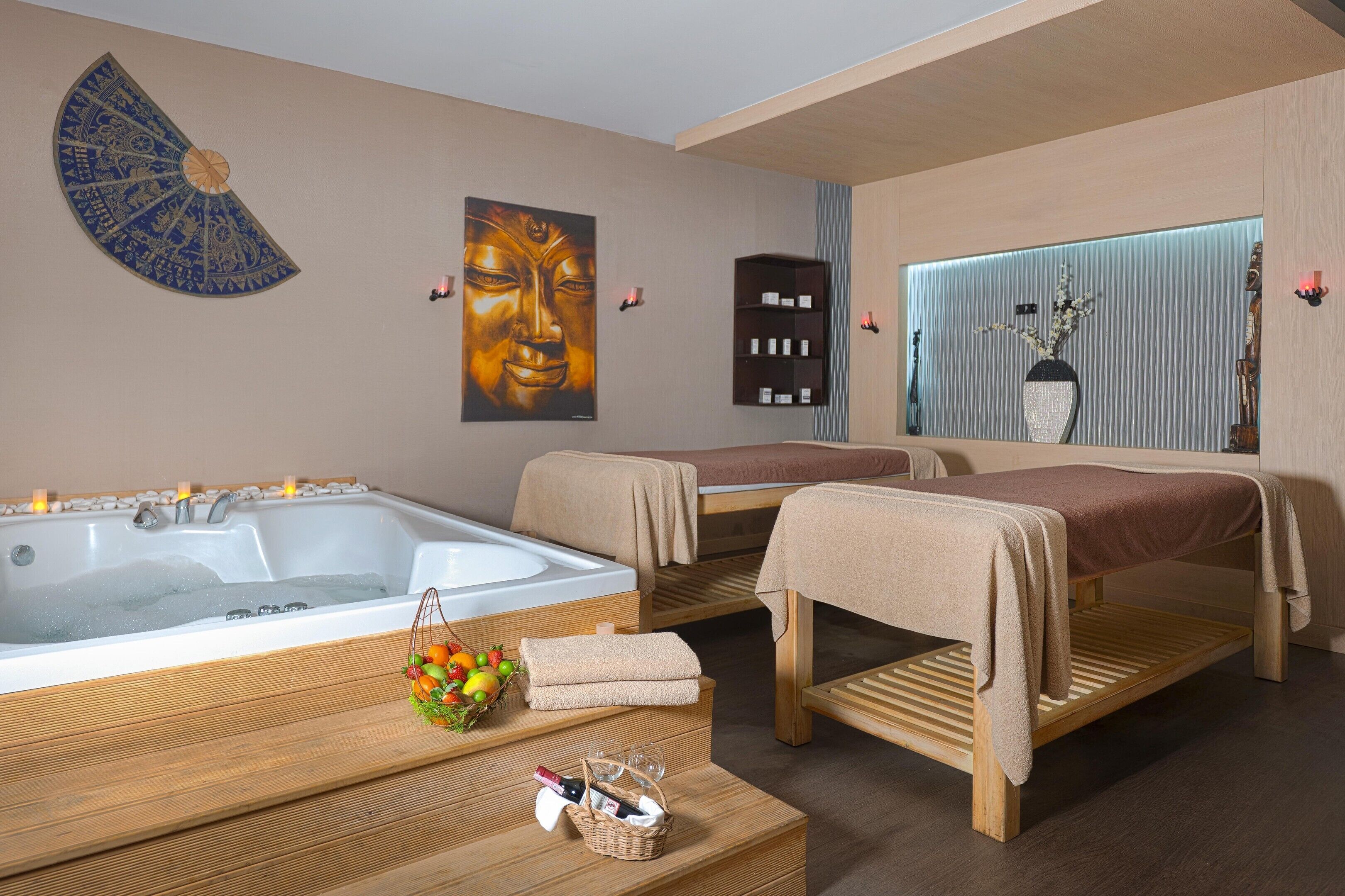 Una sala de spa con una bañera, dos camillas de masaje, un banco de madera, un estante de pared y un adorno en la pared.