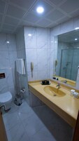 Un baño con pared de azulejos de mármol, un lavabo con espejo, un inodoro y un cubo de basura.