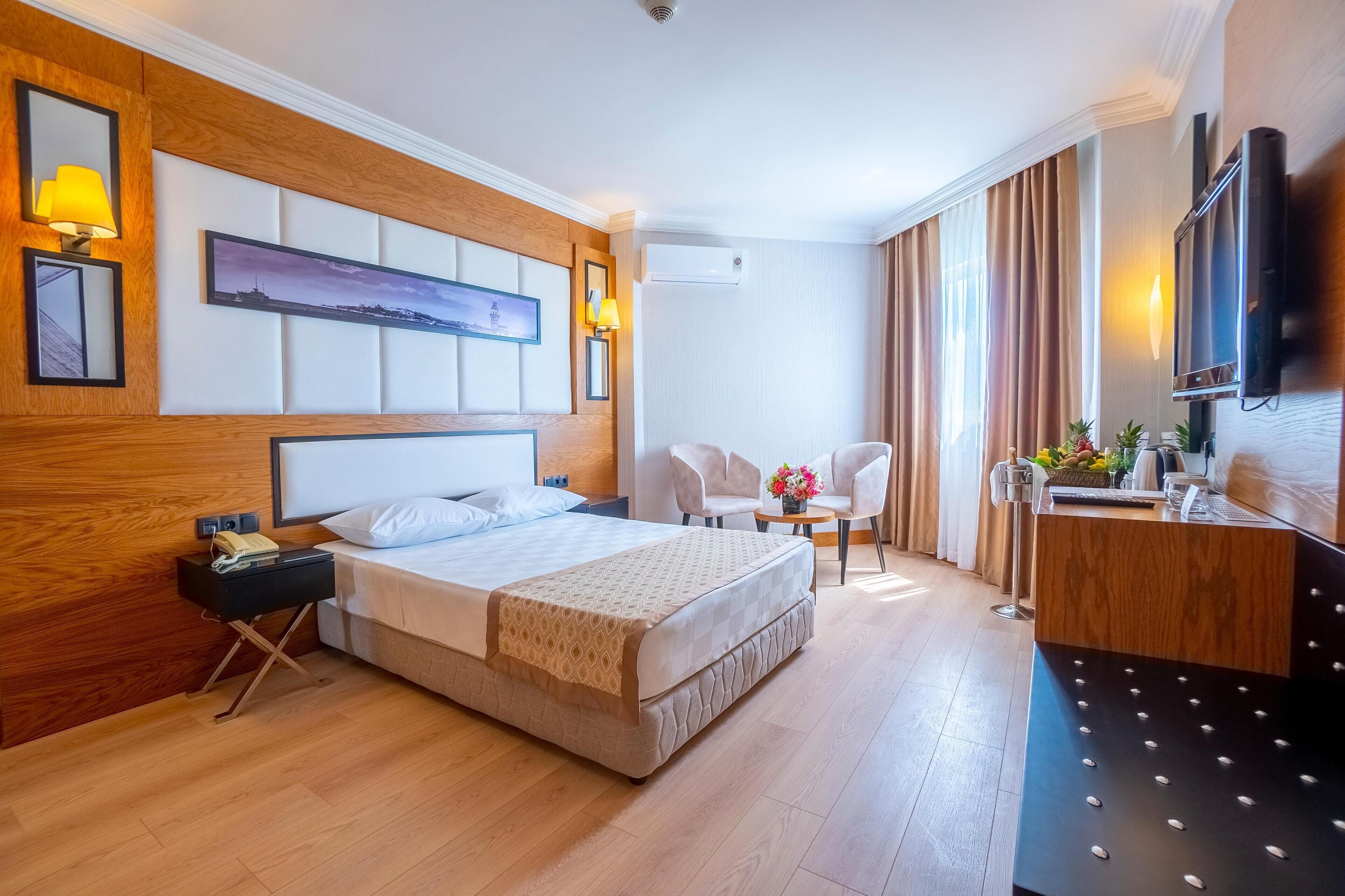 A hotel room with a large bed, bedside tables, a desk, a chair, and a TV.