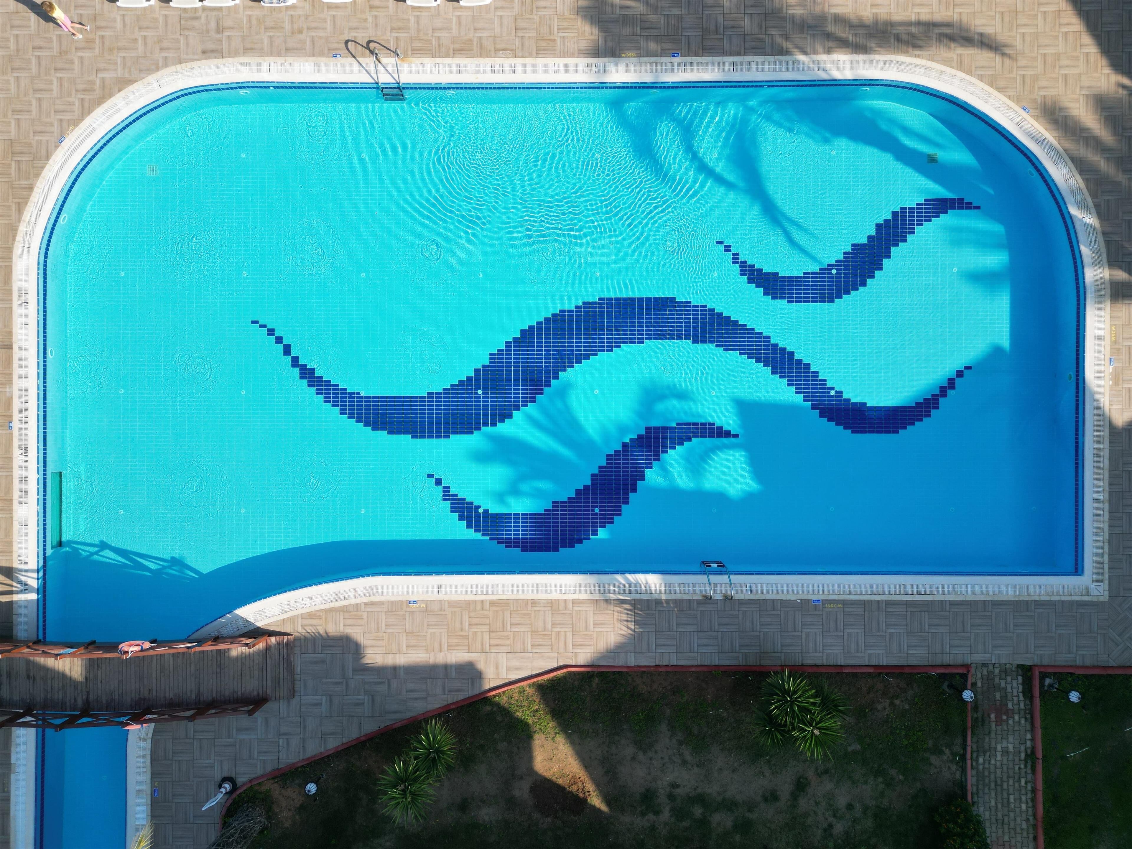 An aerial view of a rectangular swimming pool with a tiled edge and a wavy pattern in the center.