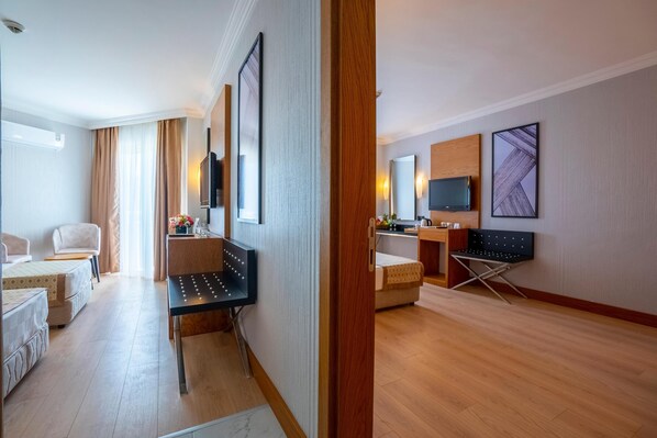 A hotel room with a sofa, a small table, a TV, and a desk with a chair. - Aydinbey Gold Dreams - Ultra All Inclusive (Alanya)