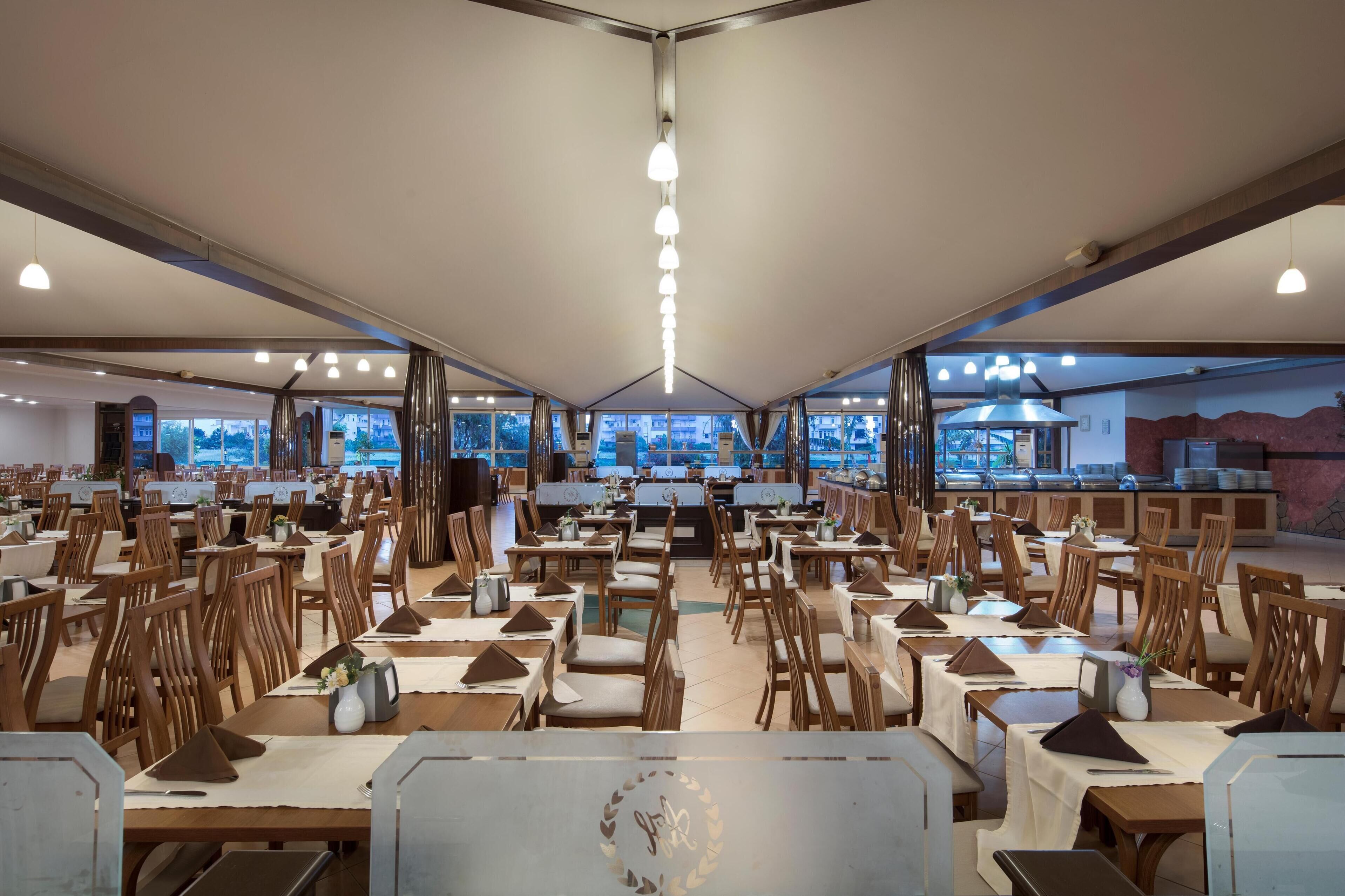 A spacious dining area with multiple tables and chairs, large windows offering a view of the outdoors, and a central counter with a menu display.