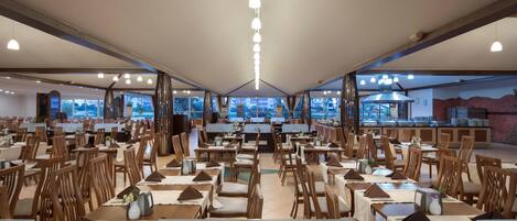 A spacious dining area with multiple tables and chairs, large windows offering a view of the outdoors, and a central counter with a menu display.