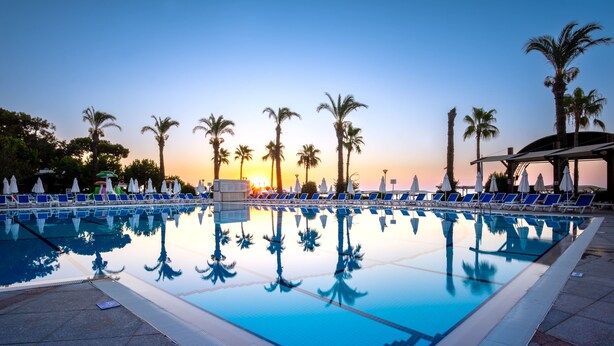 A pool with clear blue water, surrounded by lounge chairs and umbrellas, with palm trees in the background. - Mirada Del Mar Hotel - All Inclusive (Kemer)