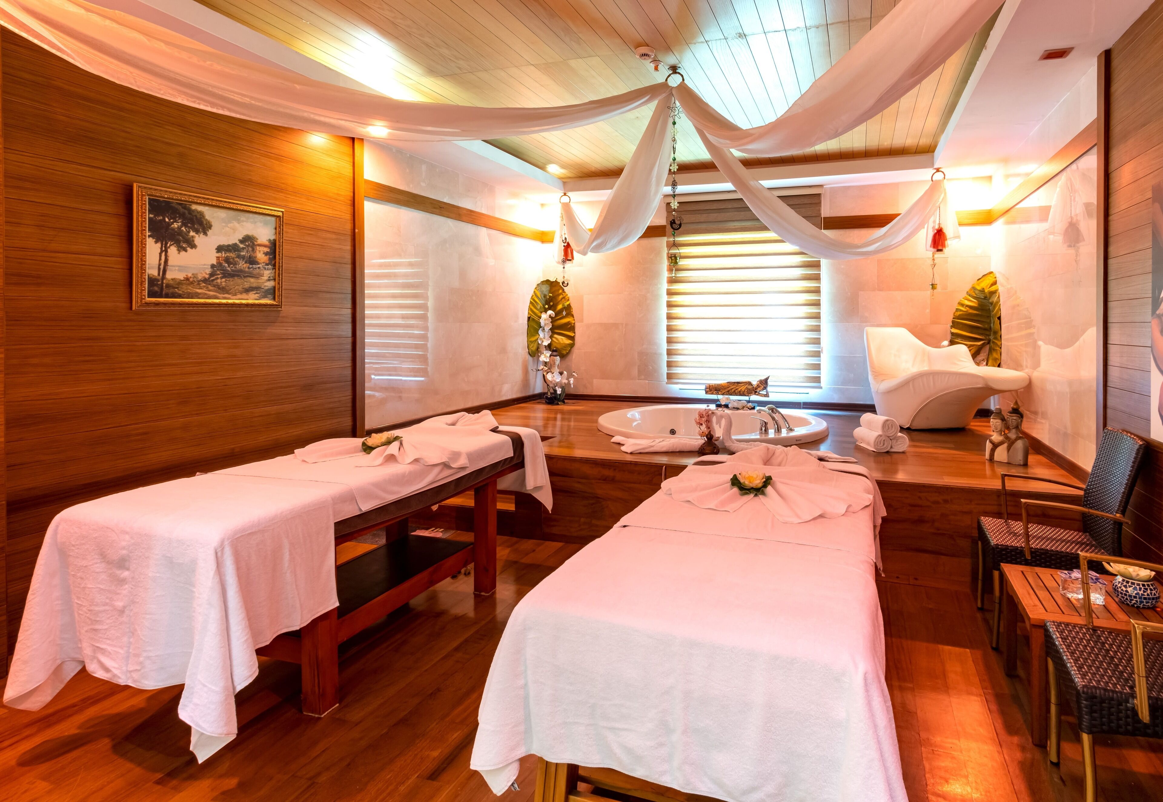 Ein Spa-Raum mit zwei Massageliegen, einer großen Badewanne und Holzboden.
