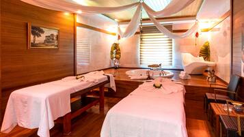 Ein Spa-Raum mit zwei Massageliegen, einer großen Badewanne und Holzboden.