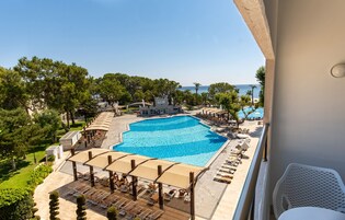 A large swimming pool with sun loungers and umbrellas, surrounded by trees and a view of the sea.