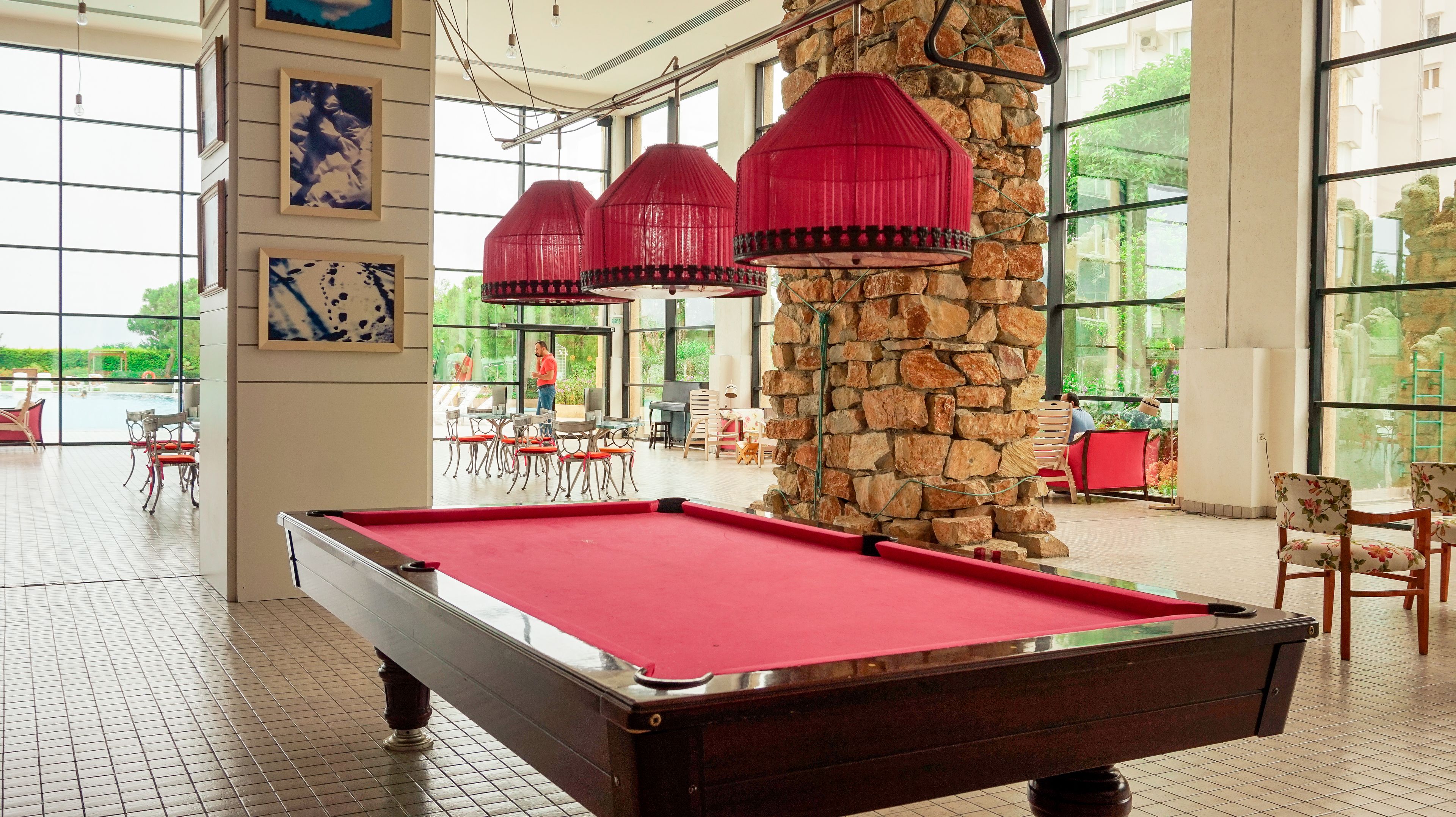 A pool table in a spacious indoor area with large windows, stone pillar, and red hanging lamps.