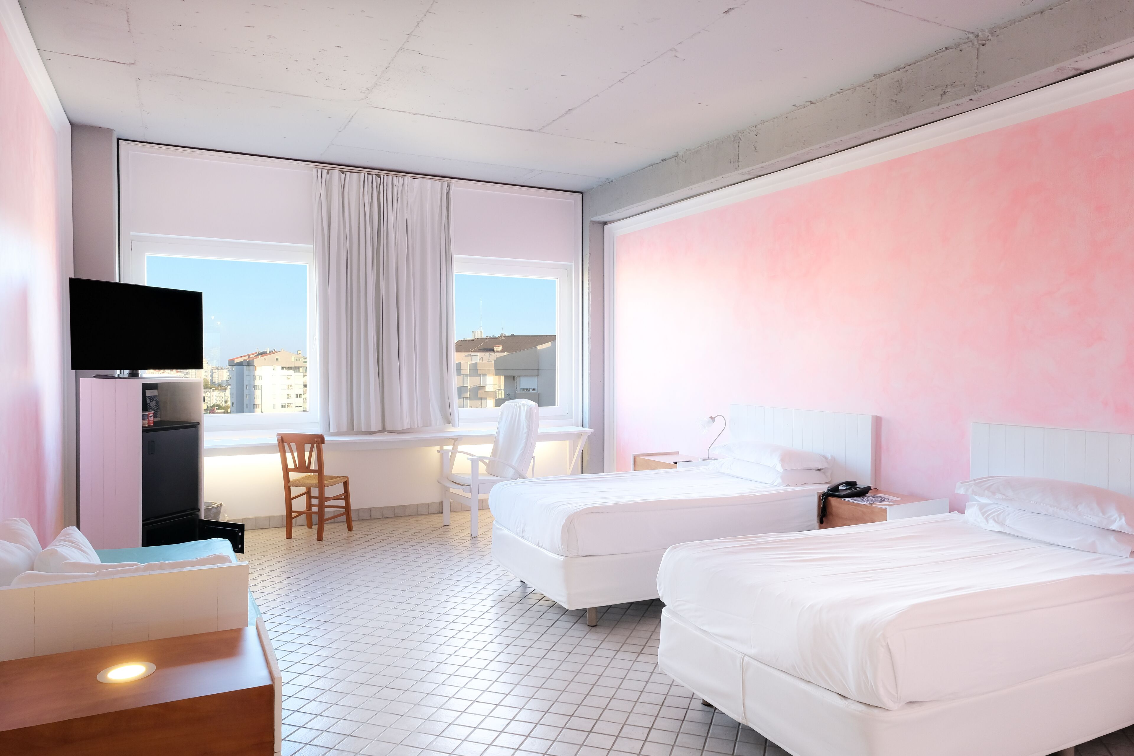 A hotel room with two beds, a desk, a chair, a TV, and a window with curtains.
