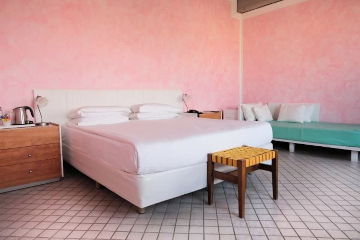 Un dormitorio con cama, mesita de noche, lámpara y un taburete de madera.