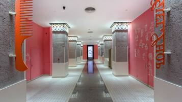 A hotel corridor with a central reflective floor, pink walls, and columns with decorative tops.
