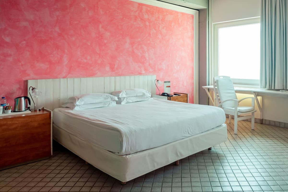 A hotel room with a large bed, a desk with a chair, a nightstand, and a window with curtains.