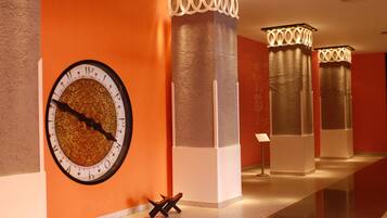 Un pasillo con un reloj de pared grande, columnas de diseños intrincados y una pequeña mesa con una silla.