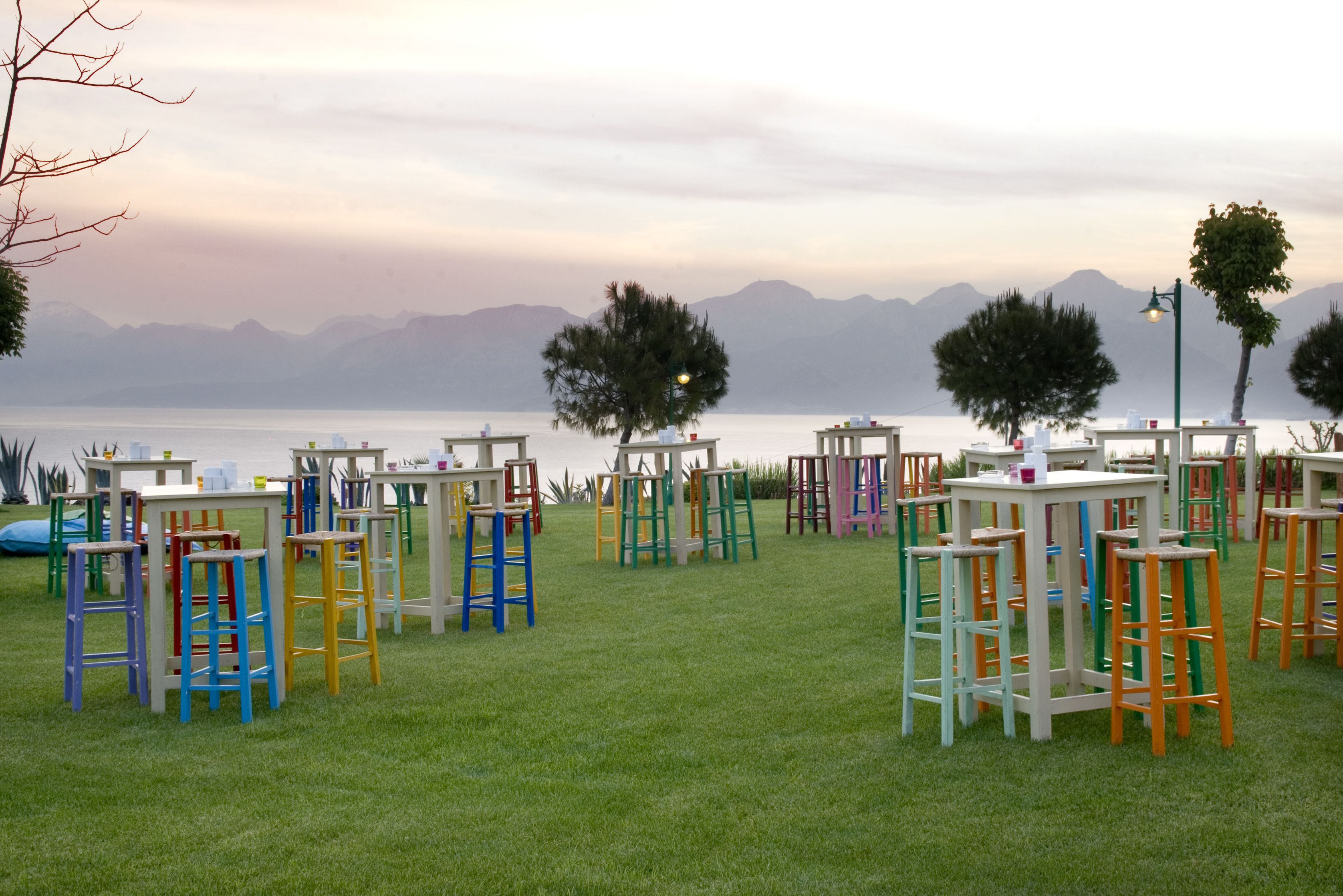 Terrasse mit Tischen und Stühlen auf einer Rasenfläche mit Blick auf Berge und ein Gewässer.