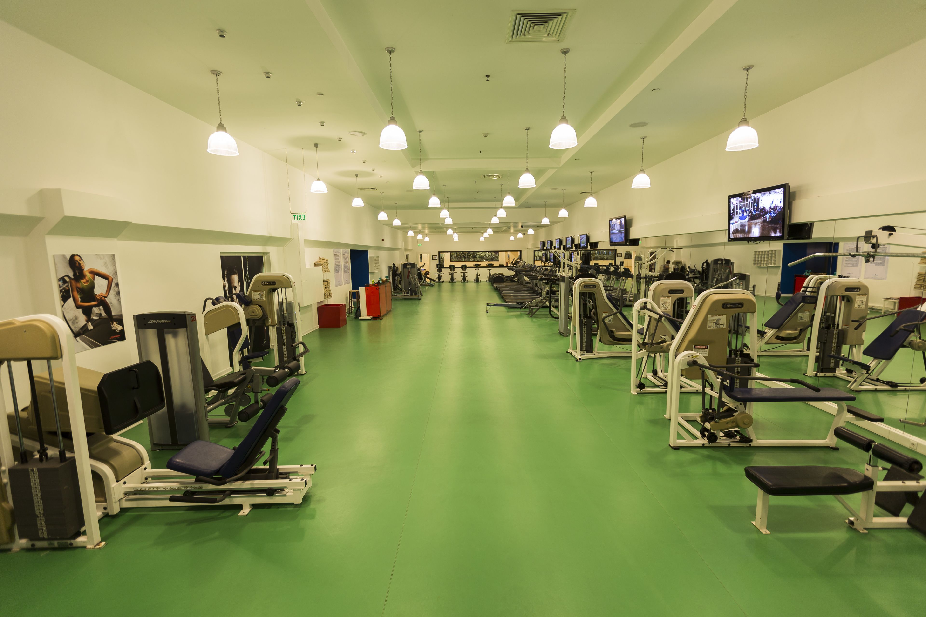A gym with various exercise equipment, green flooring, and multiple ceiling lights.