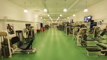 A gym with various exercise equipment, green flooring, and multiple ceiling lights.