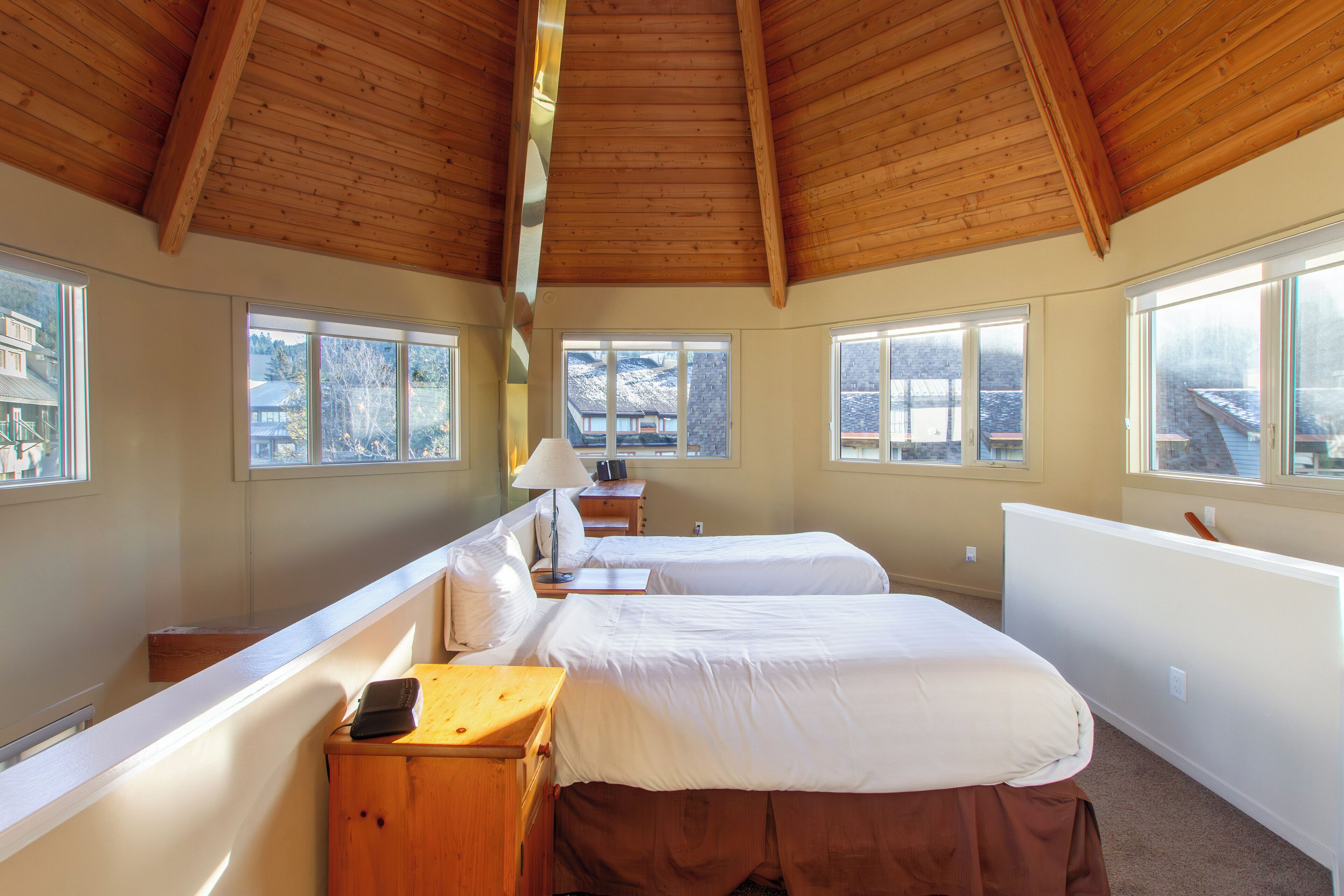 Une chambre avec deux lits, de grandes fenêtres, des poutres apparentes en bois au plafond et une vue sur une montagne.