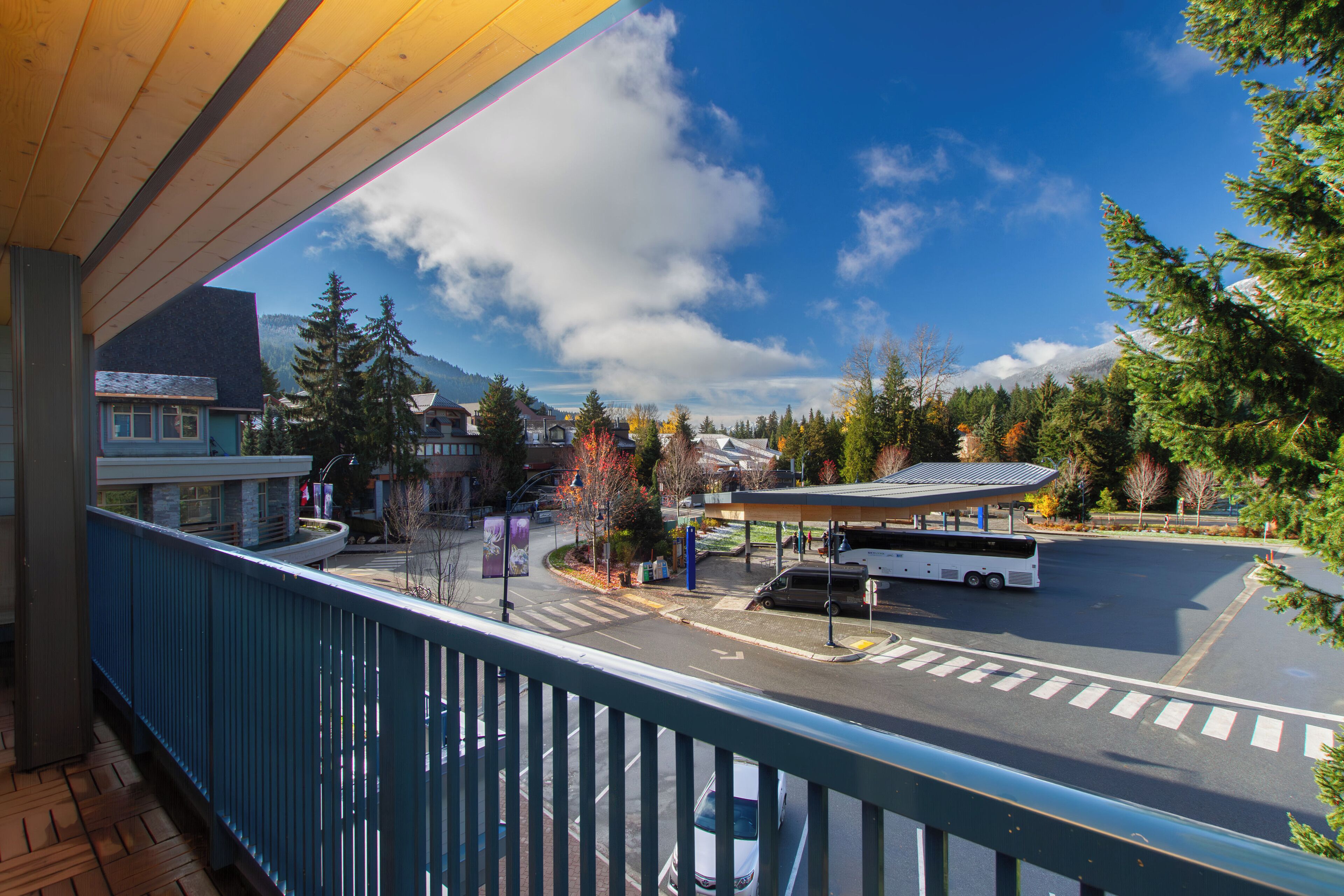 A view from a balcony overlooking a parking area with a bus, a gas station, and a mountain in the background.